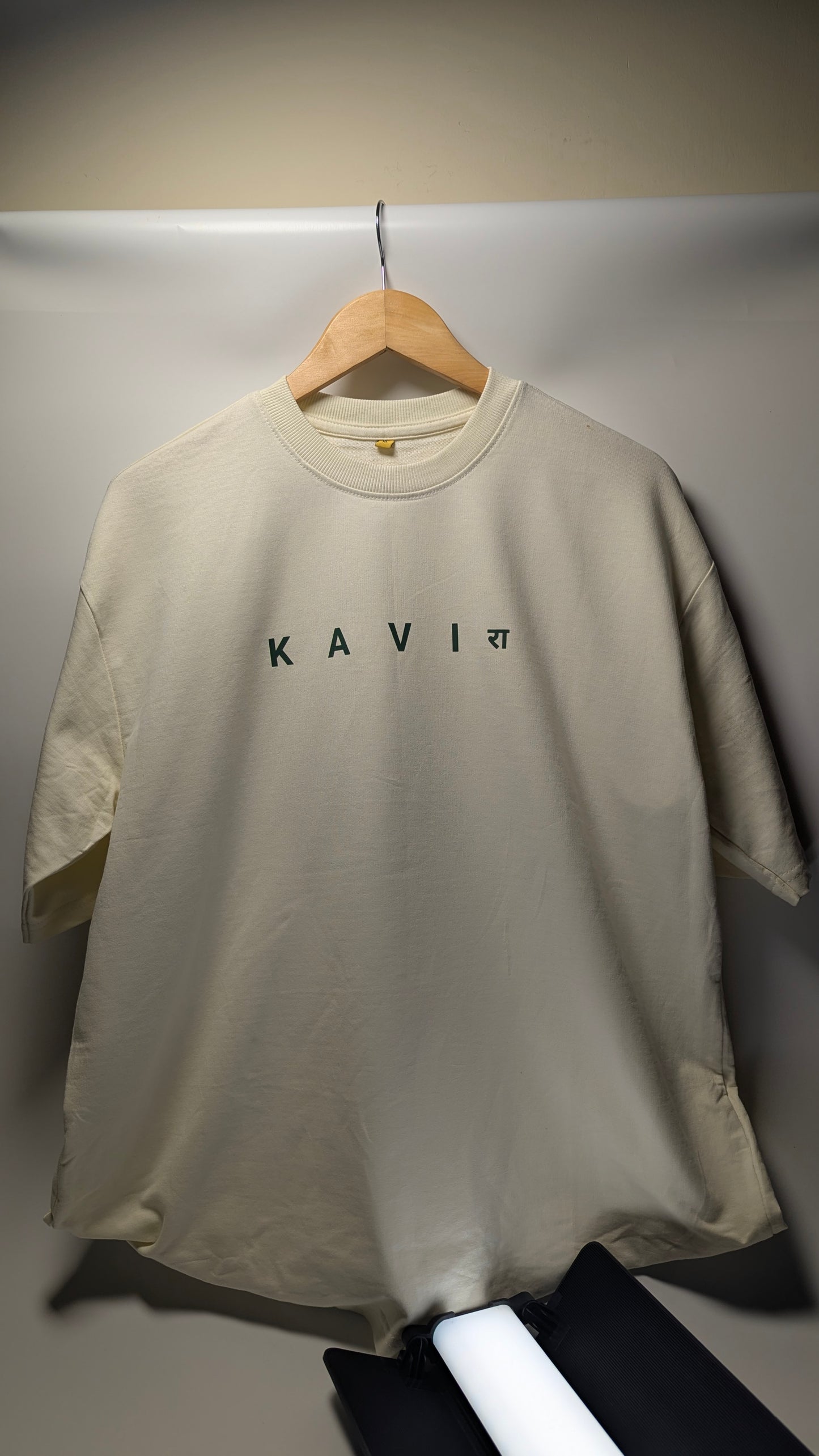 Beige t-shirt with 'KAVI' branding on a hanger.